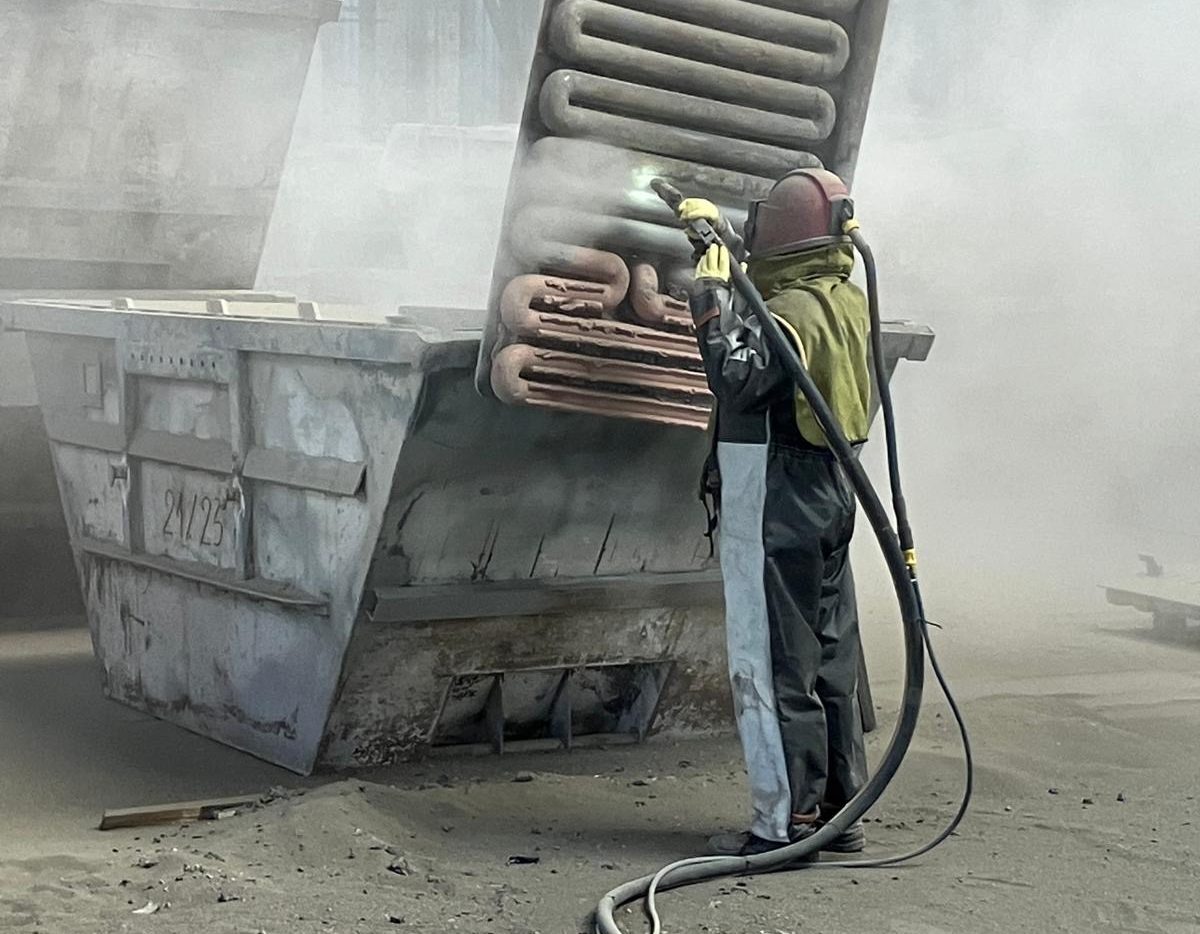 Mitarbeiter  sandstrahlt eine große Metallstruktur in einer Industriehalle